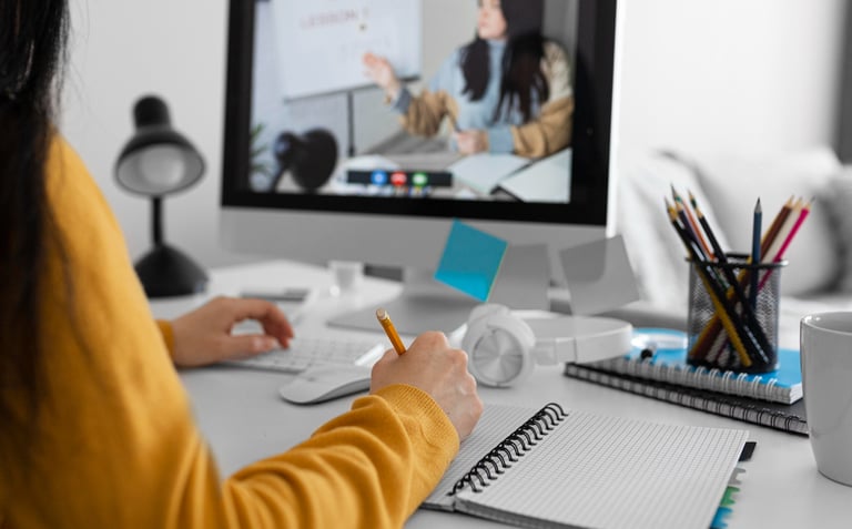 Seorang pelajar mengikuti sesi pembelajaran online dan mencatat materi sambil melihat kelas virtual di layar komputer.