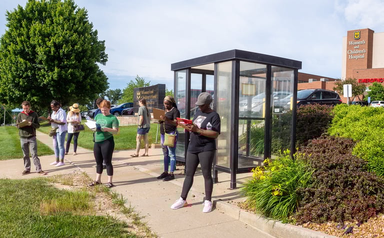 Photo of a bunch of people standing near a bus stop filling out paper surveys