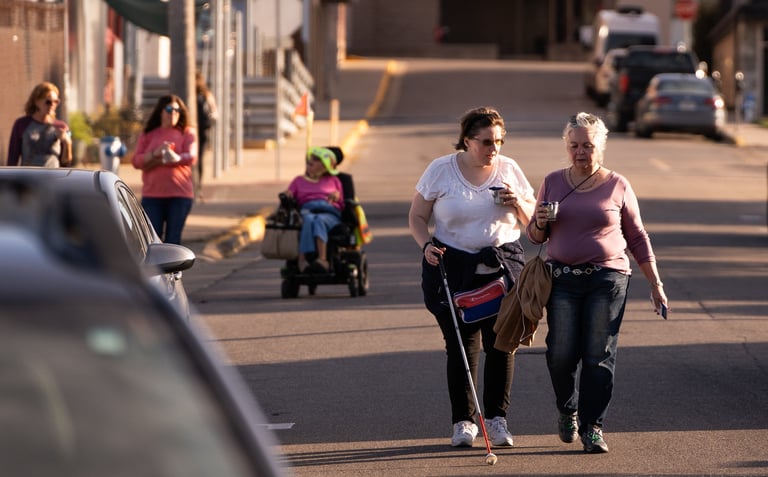 Group of people walking on the street, one in a mobility scooter, and one using a white cane