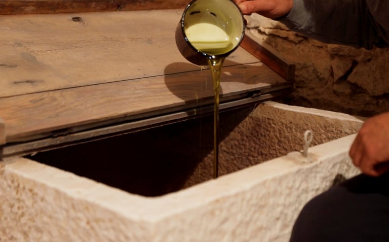 Fresh extra virgin olive oil poured from a red cup into a traditional stone storage vat.