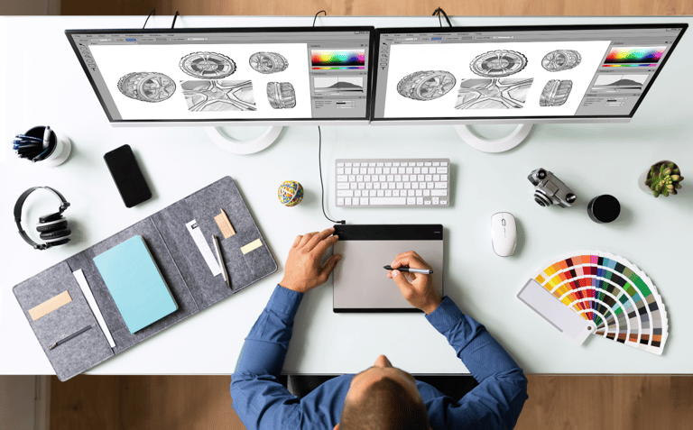 a man sitting at a desk with a laptop and a computer sketching graphics
