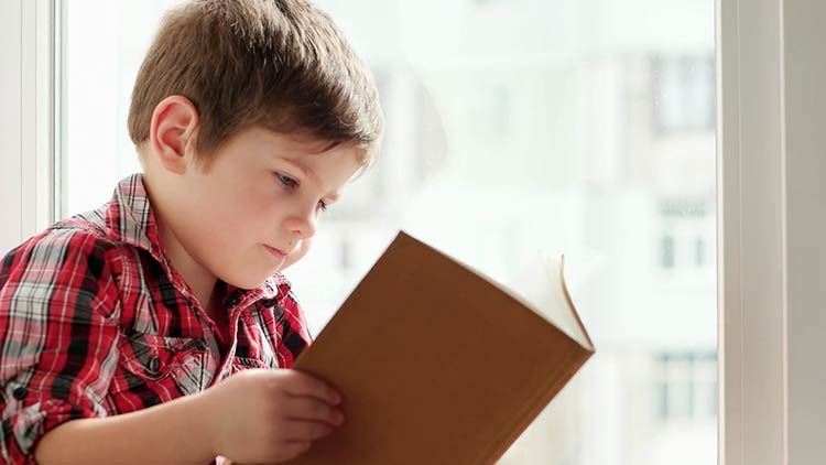 imagem de uma criança de 06 anos aproximadamente lendo um livro. 
