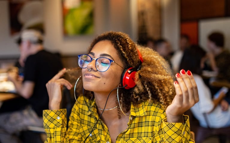 a woman in a yellow shirt with red headphones on smiling as she sits at a cafe