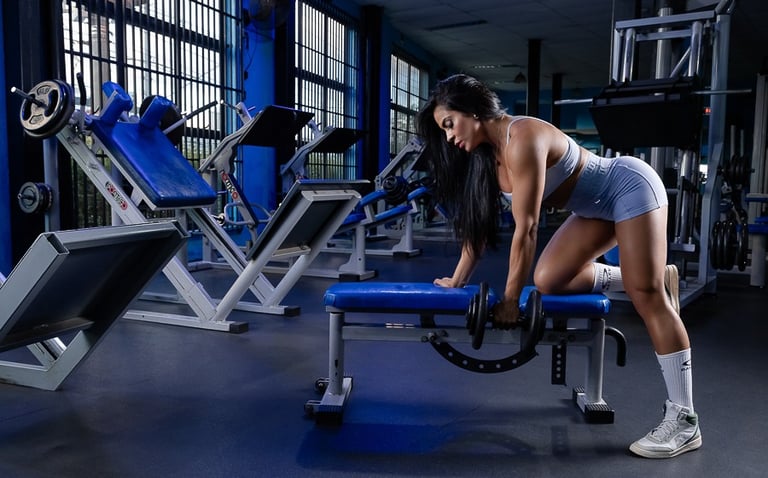 mulher cabelos longos usando o banco segurando halteres evidenciando curvas usando conjunto fitness