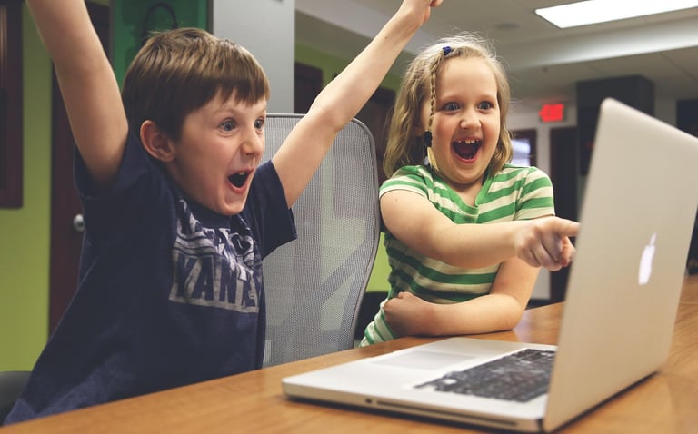 Two children happily looking at a laptop while planning a trip to Greece