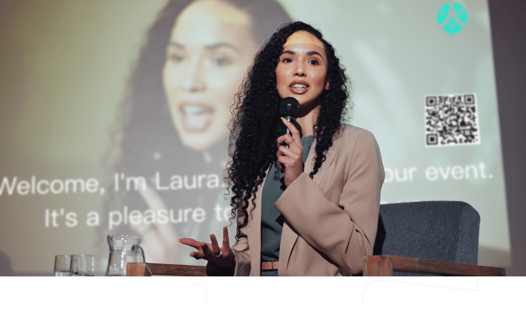 a woman in a suit and a microphone in front of a screen with Ohaio LIvesSpeaker working