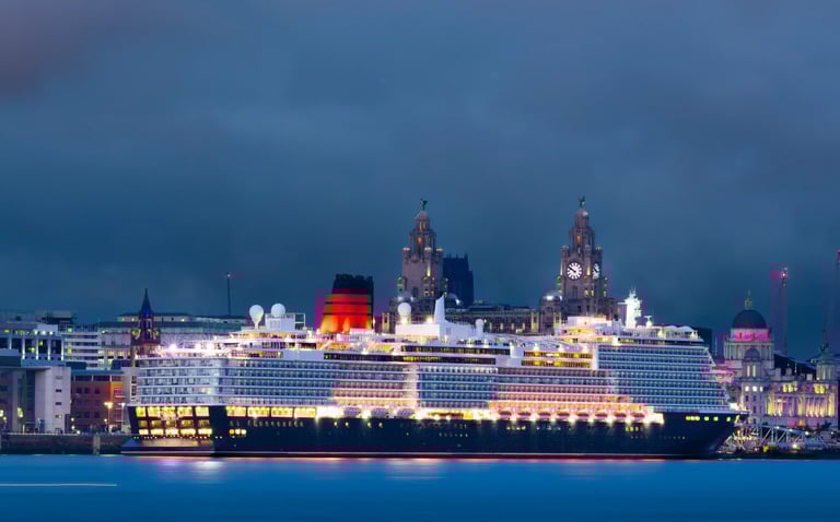 Luxury cruise ship illuminated at night at Liverpool Cruise Terminal with Liver Building in background.