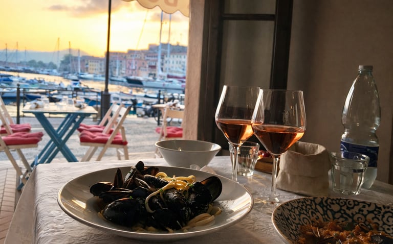 Seafood pasta with mussels and glasses of rose wine served at a waterfront restaurant at sunset.