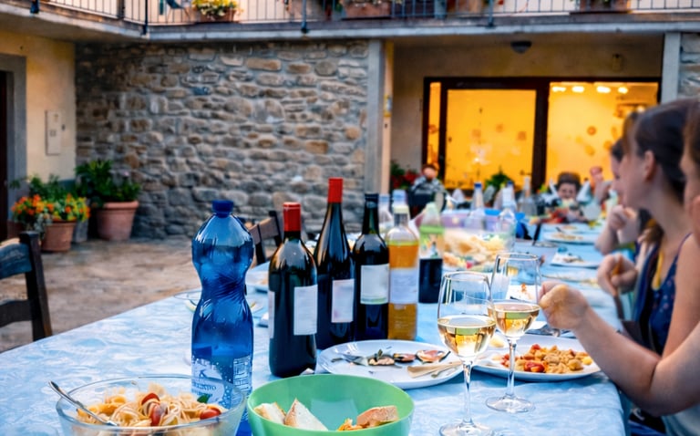Al fresco Italian dinner featuring penne pasta, wine, and bread served on a patio table at dusk.