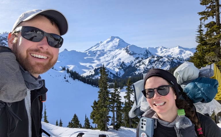 Moose and Bugs smiling in a selfie in front of snow-covered Mt. Baker on a beautiful winter day.