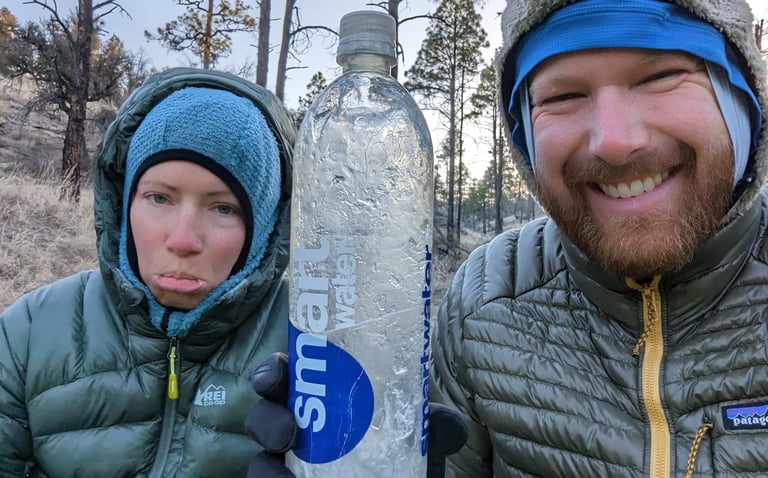 Moose and Bugs making silly faces in a selfie while Moose holds a frozen water bottle at a camp.
