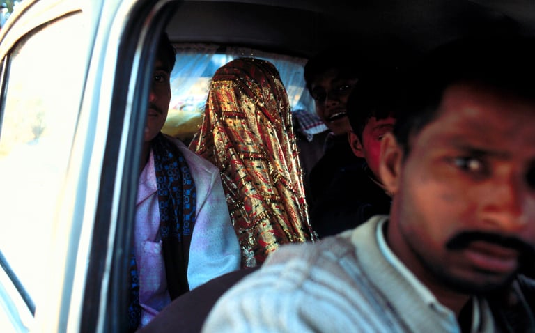 A crowded interior view of a car featuring a bride in a shimmering gold veil and other passengers looking at the camera.