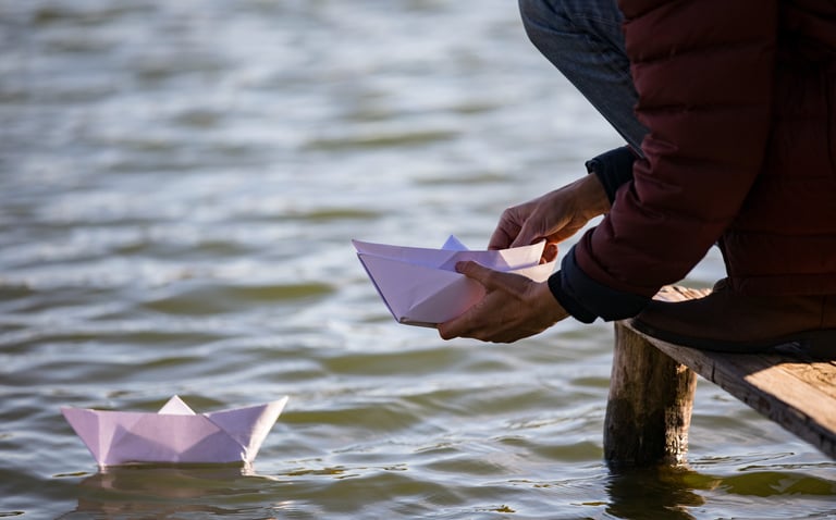 Bateau de papier flottant sur un lac, porteur d’un message symbolique d’adieu.