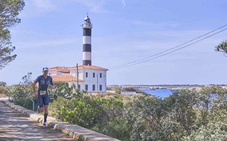 a man running on a path with a lighthouse in portocolom