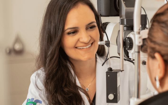 Dra Bruna Melchior de jaleco branco examinando paciente em aparelho de oftalmologia