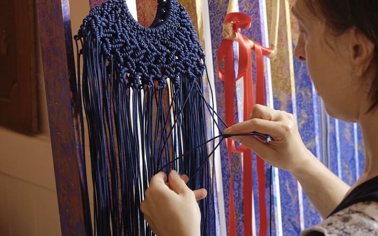 Bolsa de macramé azul marino hecha a mano siendo tejida por un artista utilizando intrincadas técnic