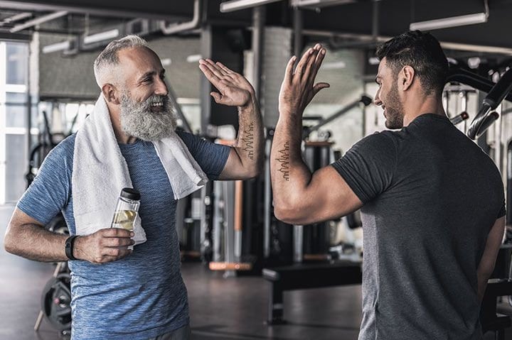 Homens se cumprimentando com high-five na academia, sorrindo após treino.