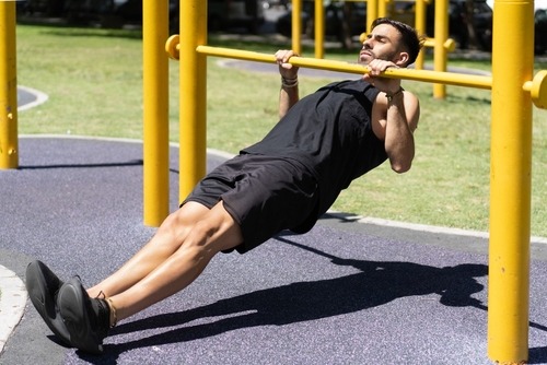 A man performing inclined bodyweight rows on yellow bars at an outdoor calisthenics park.