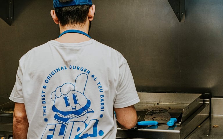 Cuiner de Flipa a la cuina amb samarreta de la marca mentre prepara burgers a la planxa