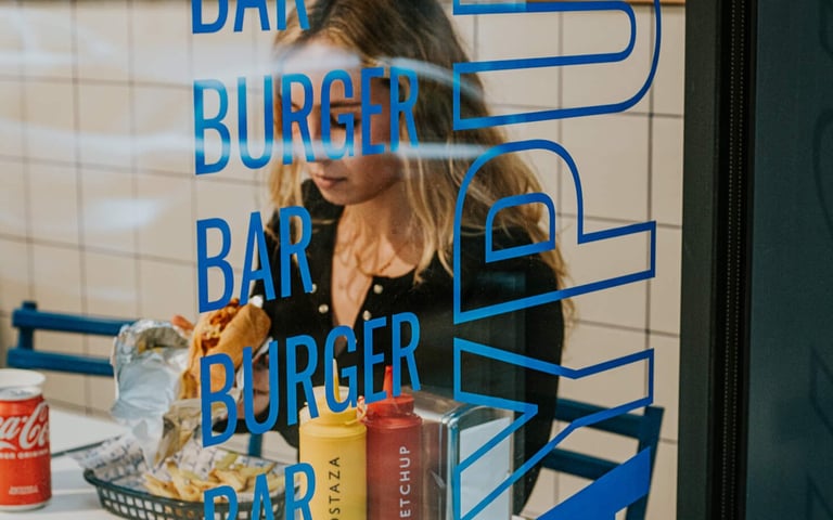 Client gaudint d’una burger a Flipa, vist a través del vidre decorat del local