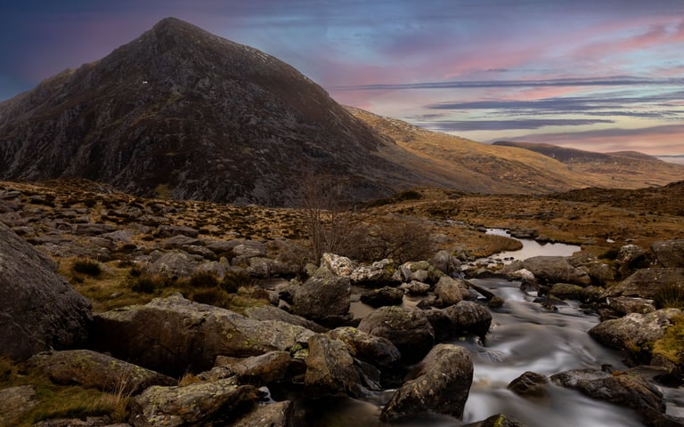 Dramatic sunset clouds over snow-capped mountains and a dark forest landscape.