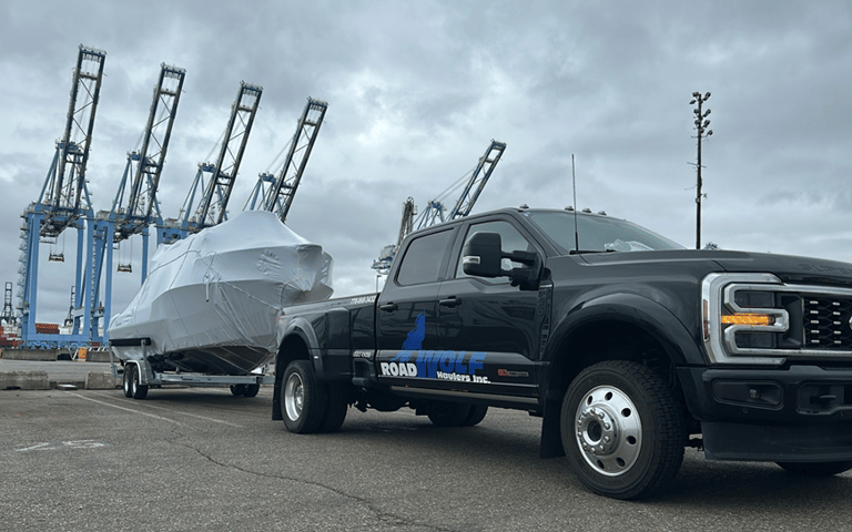 Roadwolf Haulers SuperDuty dually towing a shrink-wrapped boat on a trailer at a shipping port.