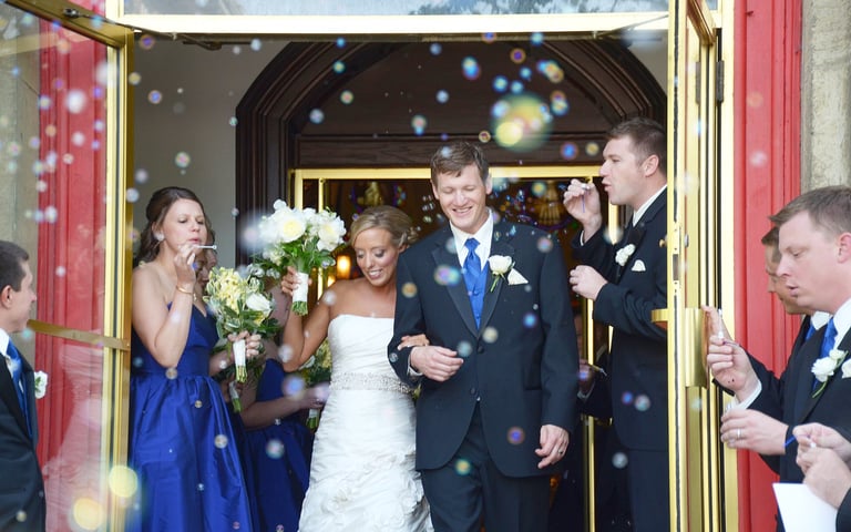 a bride and a groom are walking out of the church door with bubbles generated by guests
