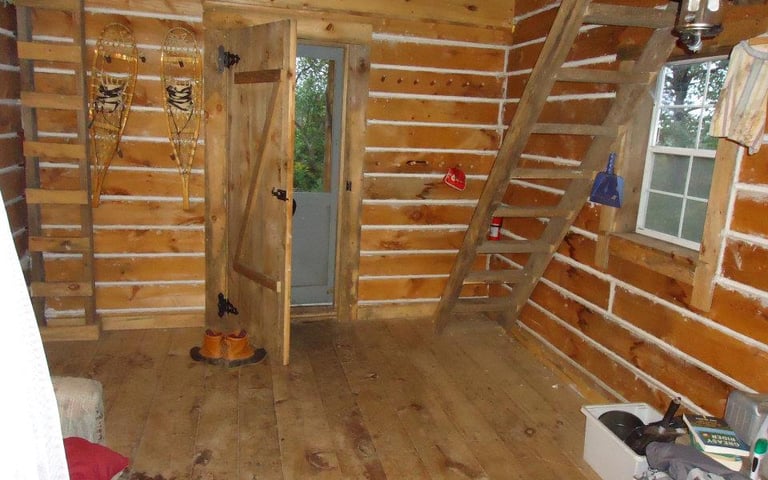 the inside of the log cabin with a ladder leading up to an unseen loft