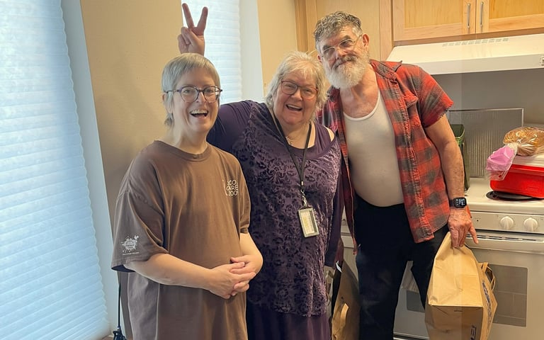 3 seniors stand together in an empty kitchen smiling and posing for the camera