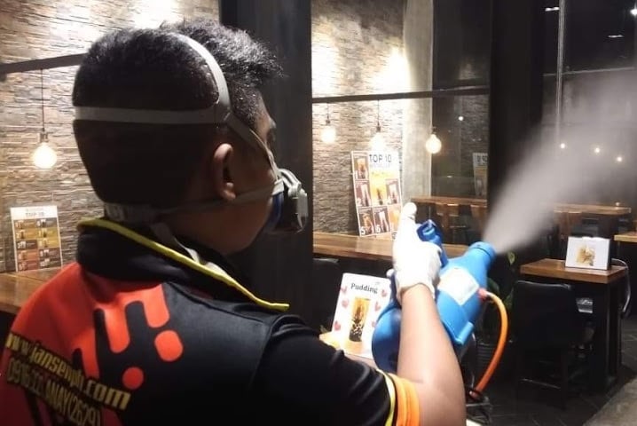 Professional pest control technician sanitizing a restaurant interior with a fogging machine and mask.