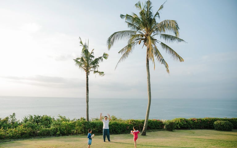 Playful sibling moment on tropical garden lawn at AYANA Villas Bali, natural family lifestyle photography