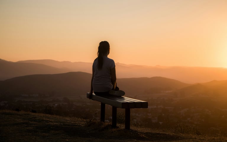 a woman sitting on a bench looking out over a valley