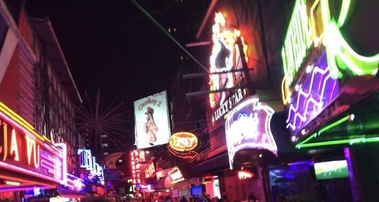 Leuchtende Neonschilder in der belebten Nachtleben-Straße Soi Cowboy in Bangkok.