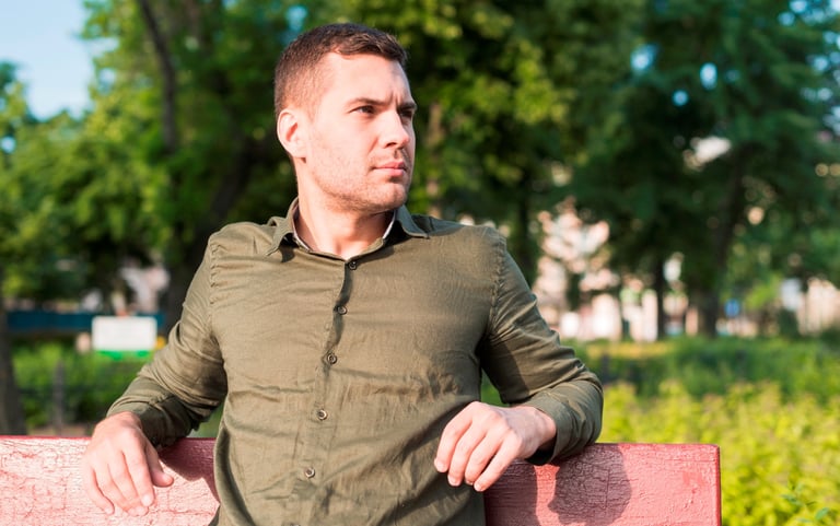 Un homme pensif assis sur un banc dans un parc arboré
