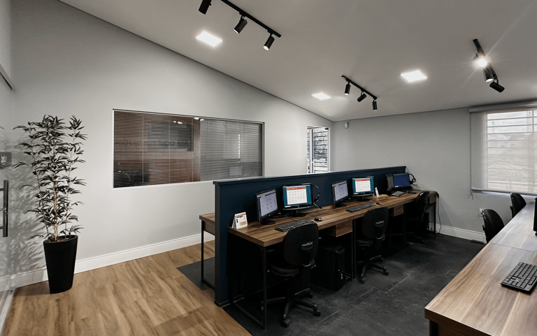 Modern office workspace with wooden desks, computer monitors, and track lighting in a minimalist call center.