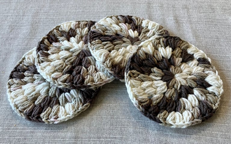 4 brown, tan, and cream crocheted drink coasters lying in a row.