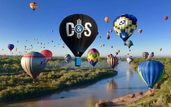Colorful hot air balloons floating over the Rio Grande river in Albuquerque during a festival.
