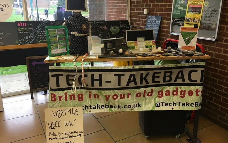 A photo of the first Tech-Takeback pop-up. A home-made banner hangs from a table covered in old tech