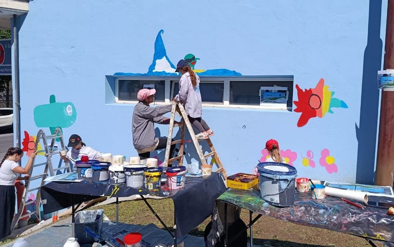 Gruppo di bambini e adulti dipinge insieme su muro azzurro durante laboratorio artistico Poliops.