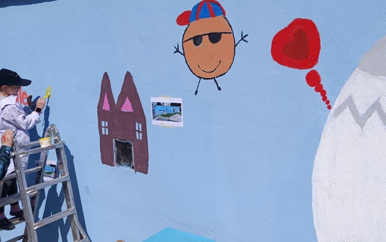 Bambini dipingono figure giocose su muro azzurro durante laboratorio artistico curato da Poliops.