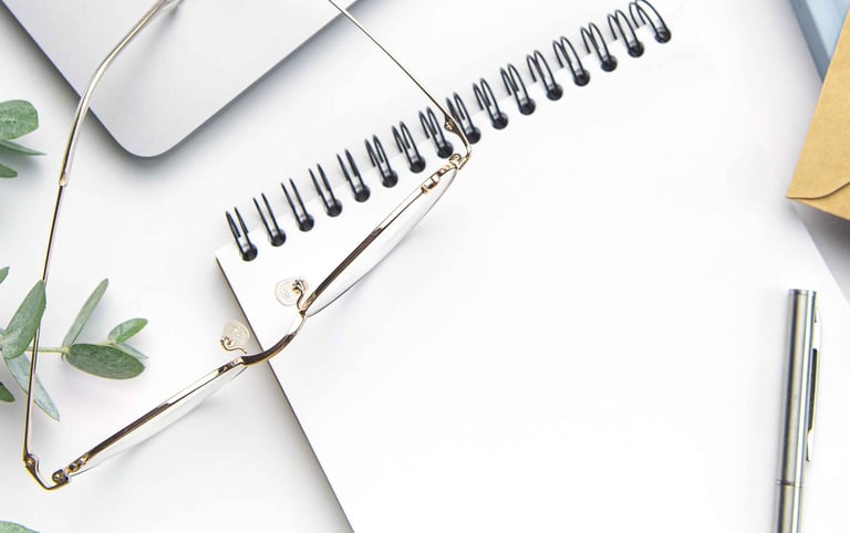 Image of a pair of glasses on top of a notepad, with a pen and a eucalyptus branch