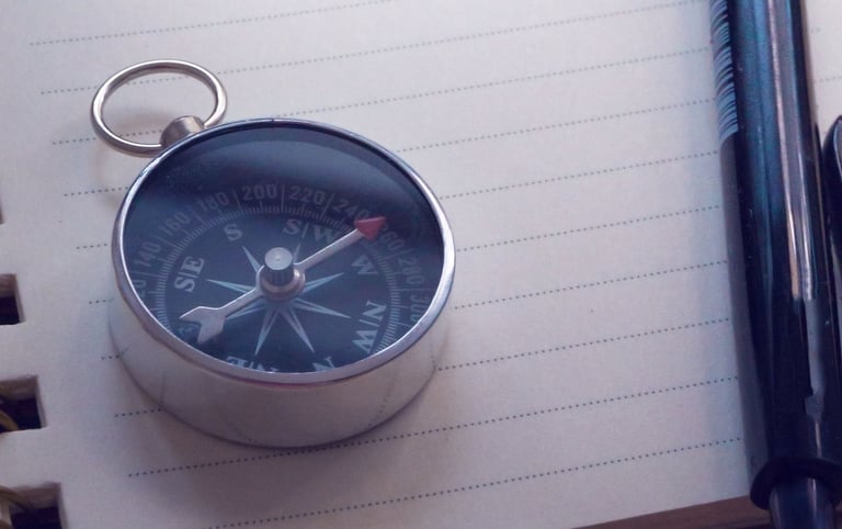 Image of compass on top of a notebook, with a pen