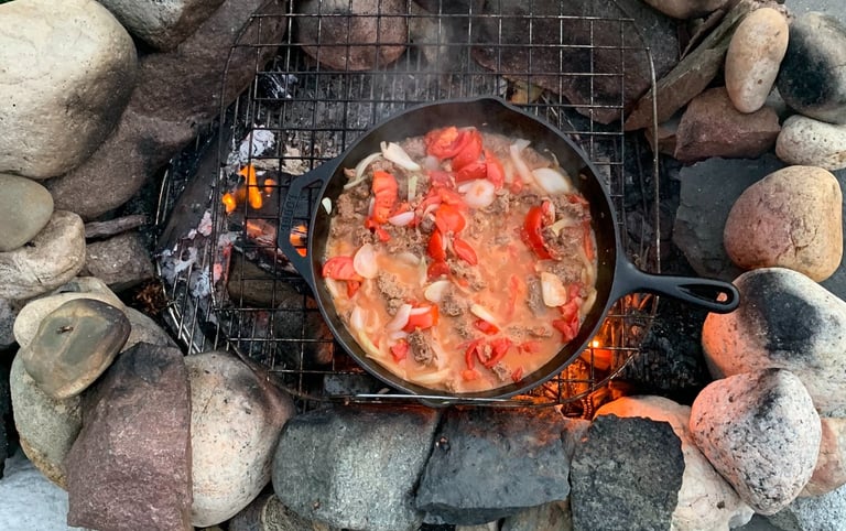 Cast iron skillet over an outdoor fire, cooking chili 
