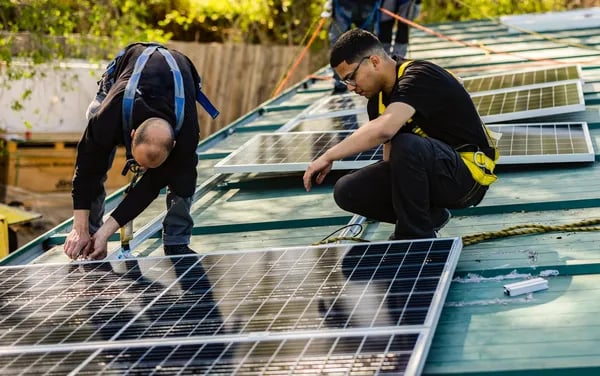 Dos hombres con camisa negra y portando equipos de protección personal trabajando en la instalación