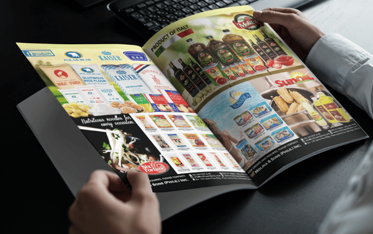 a person holding a magazine in front of a laptop