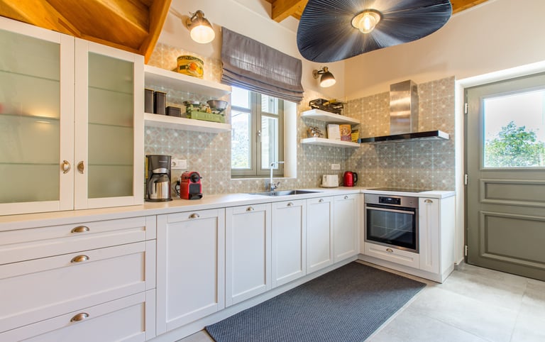 Bright kitchen with white cabinets, modern appliances, and door to garden at Villa Skyphos