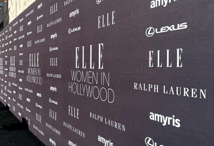 a woman in a black dress standing in front of a wall with a large sign