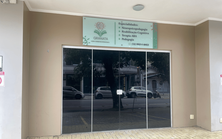 Fachada da Clínica Granata com porta de vidro espelhada e placa de identificação verde. Na placa, lêem-se as especialidades.