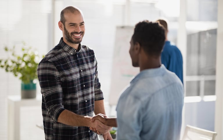 A smiling businessman shaking hands with a colleague in a bright office setting.
