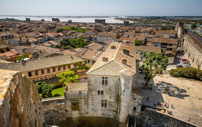 Aerial view of Aigues-Mortes medieval walled city in France with stone buildings and salt pans in the distance.